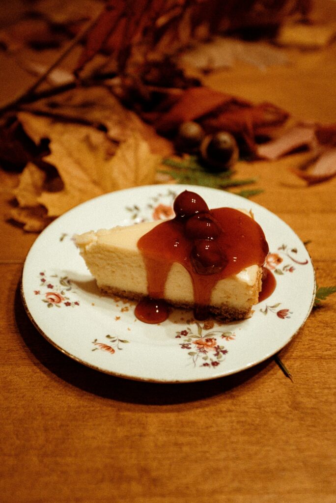 Close-up of a cheesecake slice topped with cherry sauce on a floral plate, ideal for food photography.