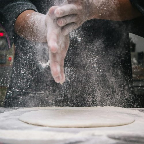 A chef clapping hands over dough, releasing flour in a kitchen setting.